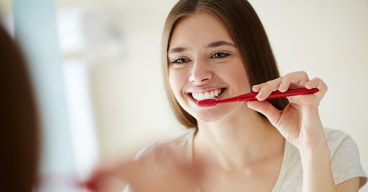 woman brushing her teeth with a red toothbrush and making health dental choices woman brushing her teeth