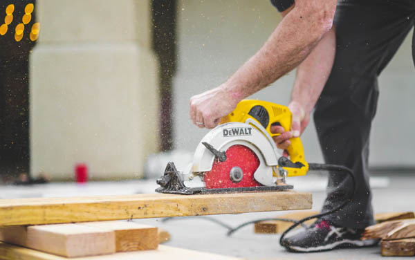 a married man wearing Asics shoes is using a DeWalt skill saw